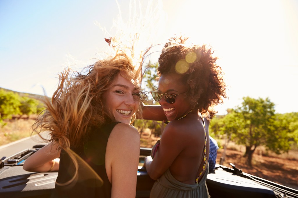 Duas amigas andando de carro conversível com o cabelo ao vento