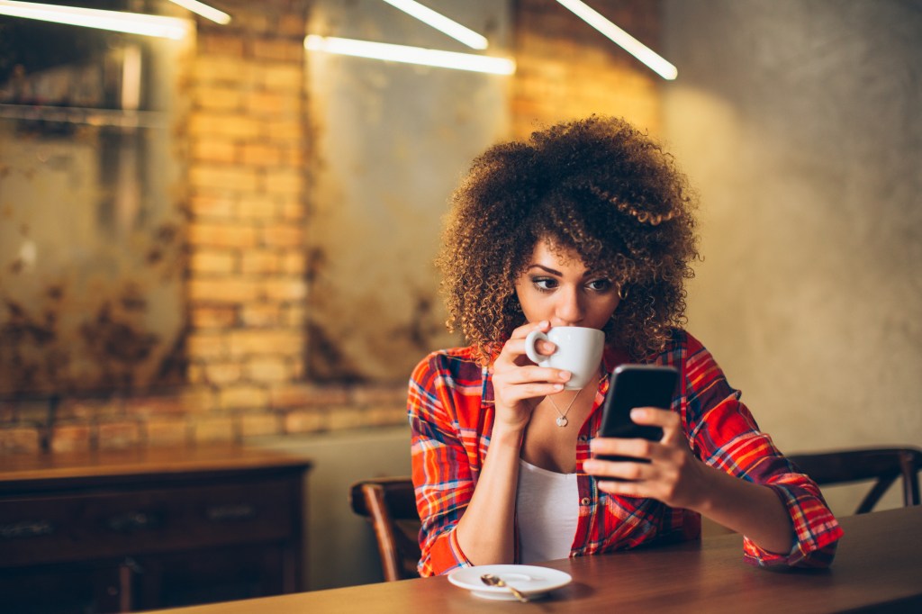 Mulher negra tomando café e olhando o celular