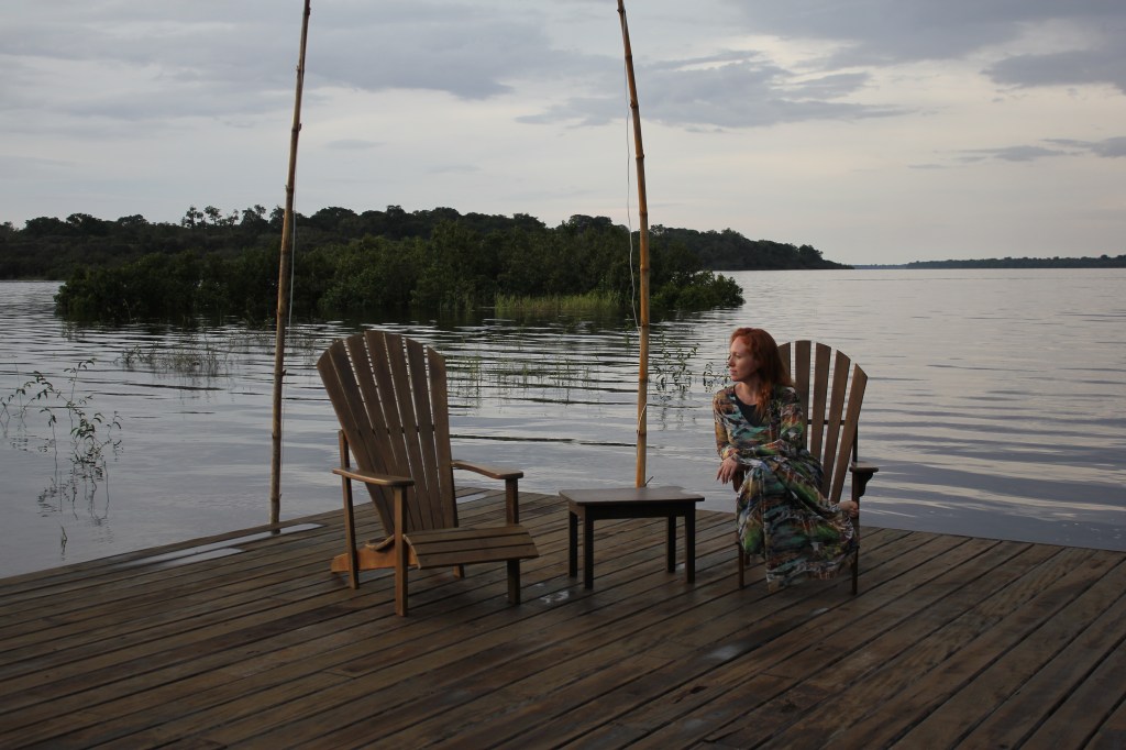 Cacá Filippini sentada em uma cadeira de madeira ao entardecer no pier do hotel Mirante do Gavião