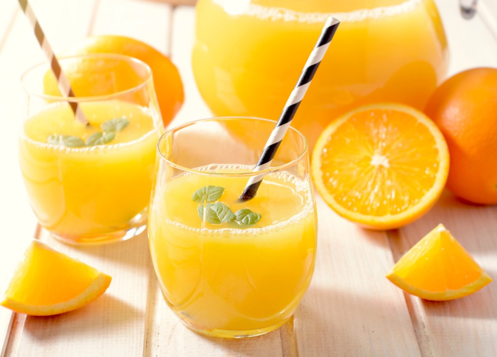 Jarra de suco de laranja com várias frutas cortadas e dois copos com canudo