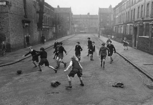 Foto antiga em preto e branco de crianças inglesas jogando uma partida de futebol na rua