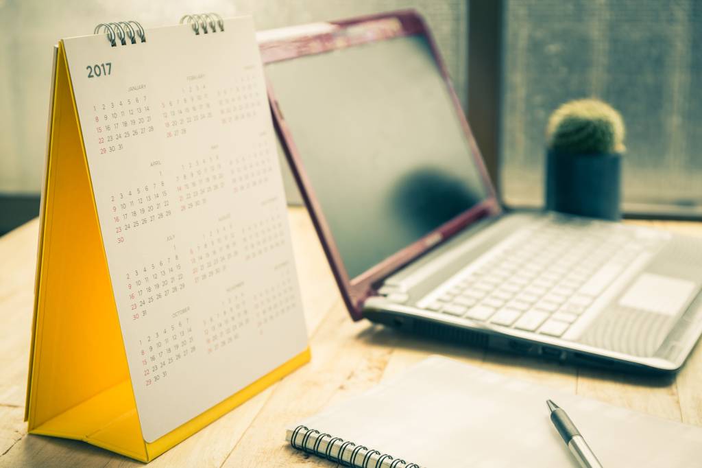 Uma mesa com um laptop, um calendário de 2017 e um caderno com uma caneta em cima